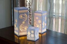 two white paper lanterns sitting on top of a wooden table next to a curtained window