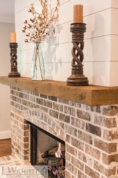 a brick fireplace with two candles and a vase filled with flowers on the mantel