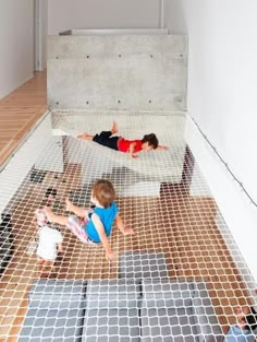 two children are playing on the floor in a room with mesh netting and wood floors