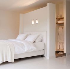 a white bed sitting in the middle of a bedroom next to a wall mounted shelf