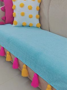 a blue couch with yellow and pink pom poms on the backrests