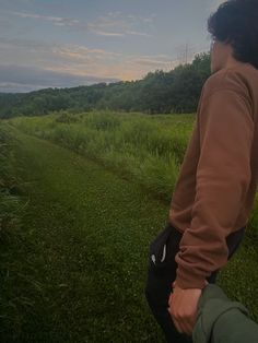 a man holding the hand of another person in a grassy field with trees and sky in the background