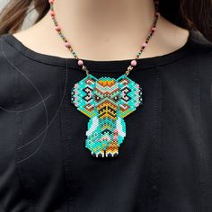 This large handmade necklace is a tribute to ethnic art, featuring a stunning elephant design in turquoise tones complemented by shades of brown, yellow, and pink. Each piece is meticulously crafted from fine Japanese Delica beads, with the chain adorned in Delica beads and delicate pink stones, adding to its boho allure. Ideal for those seeking vibrant accents and wishing to infuse their attire with an artistic bohemian flair, this necklace is a standout piece that embodies creativity and cultu Handmade Bead Jewellery, Bead Loom Designs, Beaded Art, Original Necklace, Artisan Fashion, Elephant Necklace, Coral Earrings, Halloween Earrings, Art Colorful