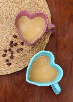 two heart shaped mugs sitting on top of a wooden table next to a straw hat