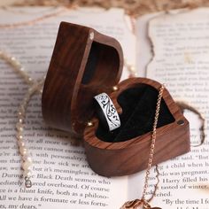 an open wooden box with a ring inside on top of a book that is sitting on a table