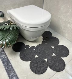 a white toilet sitting on top of a bathroom floor next to a plant and rug