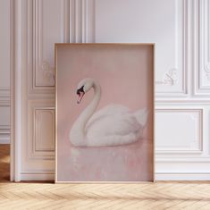 a white swan sitting on top of a wooden floor in front of a pink wall