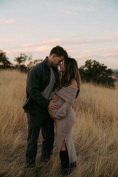 a pregnant couple standing in tall grass at sunset