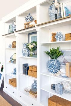 a white bookcase with blue and white vases on it's shelves in a living room