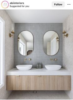 two round mirrors are above the double sinks in this modern bathroom with wood cabinetry and white countertops