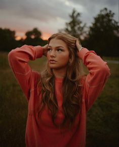 a woman with long hair is standing in the grass and has her hands on her head