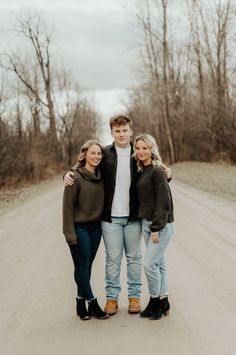 three people standing in the middle of a dirt road