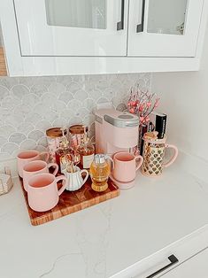 the kitchen counter is covered with pink coffee cups and mugs, along with other items