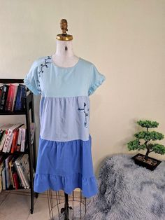 a dress on a mannequin in front of a book shelf and a bonsai tree