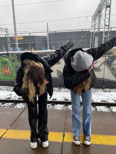 two people standing on a train platform with their arms in the air