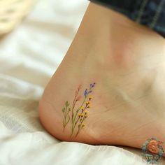 a small tattoo on the foot of a woman with wildflowers growing out of it