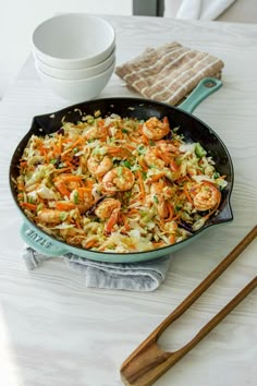 a skillet filled with shrimp and rice next to chopsticks on a table