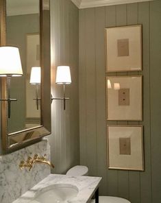 a white toilet sitting next to a bathroom sink under a vanity with two lamps on top of it