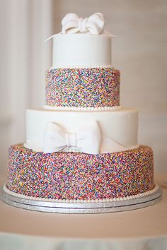 a three tiered cake with sprinkles and bows on it's sides