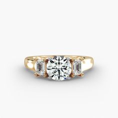 a three stone engagement ring in yellow gold with two diamonds on the side and an oval diamond