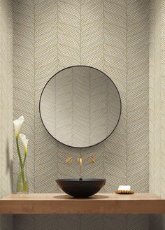 a bathroom sink sitting under a mirror on top of a wooden counter next to a vase with flowers