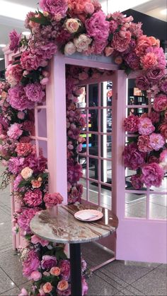 a pink door with flowers on it and a table in front of the door that has a glass window