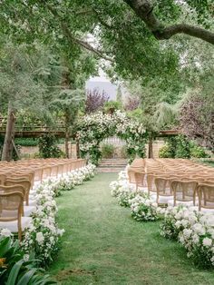 an outdoor ceremony set up with chairs and flowers on the grass, surrounded by trees