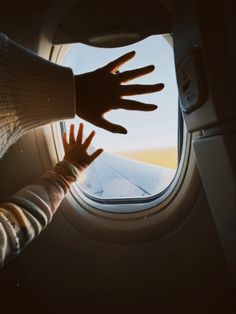 a person reaching out an airplane window to catch something in the air with their hands