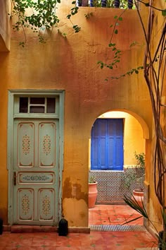 an orange building with a blue door and window on the outside, in front of a tree