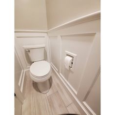 a white toilet sitting in a bathroom next to a roll of toilet paper on the wall