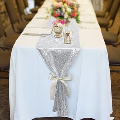 the table is decorated with silver sequins and white linens, as well as flowers