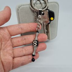 a hand holding a keychain that has the letter s on it and is attached to a metal chain