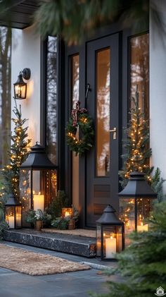 christmas wreaths and lit candles are on the front steps of a house with evergreen trees