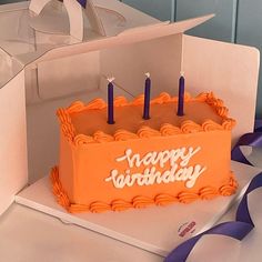 an orange birthday cake with blue candles on it sitting in front of a white box