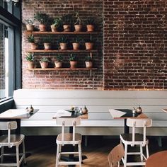 the interior of a restaurant with tables and chairs in front of a brick wall that has potted plants on it