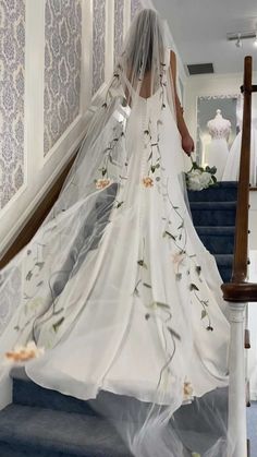 the bride is walking down the stairs in her wedding dress with flowers all over it