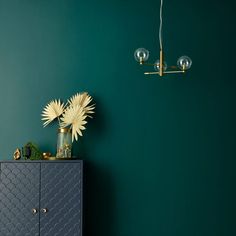 a room with green walls and a blue cabinet next to a flower vase on the floor