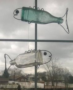 two fish shaped glass bottles hanging from the side of a window with cloudy skies in the background