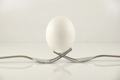 an egg sitting on top of a fork next to a white object that is shaped like a cross