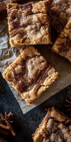 several pieces of brownie sitting on top of paper next to cinnamon sticks and star anise