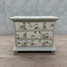 a white dresser with flowers painted on it's sides and drawers in front of a wall