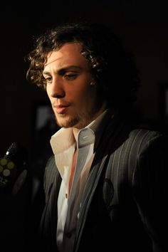 a man with curly hair wearing a suit and holding a microphone in front of him