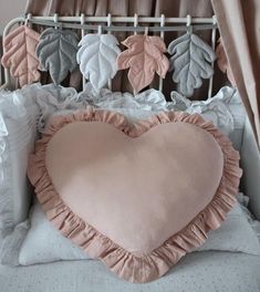 a heart shaped pillow sitting on top of a bed next to pillows and sheets with leaves