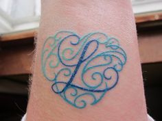 a blue tattoo on the wrist of a person with a heart shaped monogramm