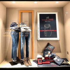 two pairs of jeans are on display in a store window with shoes and other items