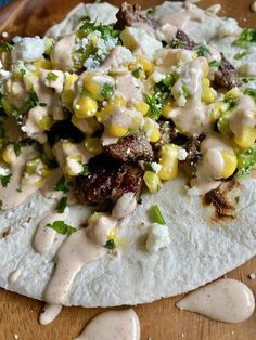 a tortilla topped with corn, meat and dressing on top of a wooden cutting board