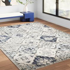 a white and blue area rug in a living room with hardwood flooring, windows, and artwork on the wall