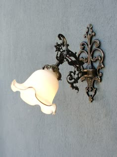 an ornate wall light with a white glass shade on it's arm, against a blue background