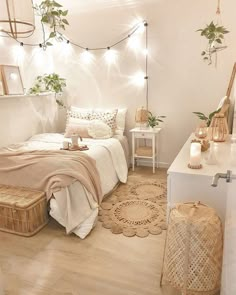 a bedroom with white walls and string lights on the ceiling, a bed covered in pink blankets