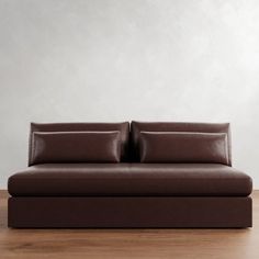 a brown leather couch sitting on top of a wooden floor next to a white wall